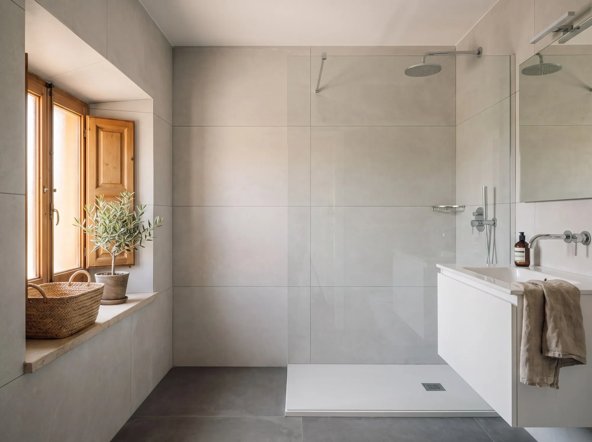 Salle de bain rénovée avec grands carreaux gris clair et paroi de douche vitrée